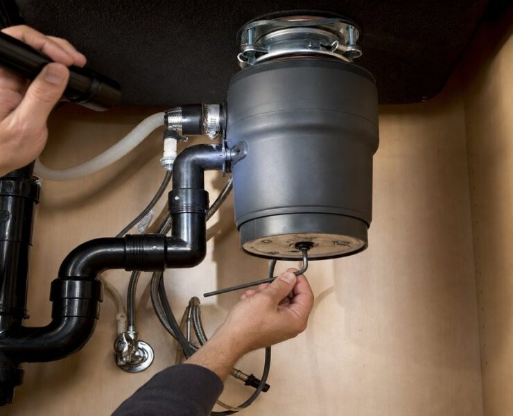 Using a hex wrench to free a jammed garbage disposal under a kitchen sink