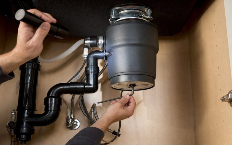 Using a hex wrench to free a jammed garbage disposal under a kitchen sink