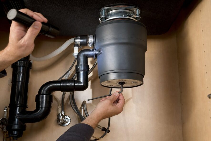Using a hex wrench to free a jammed garbage disposal under a kitchen sink